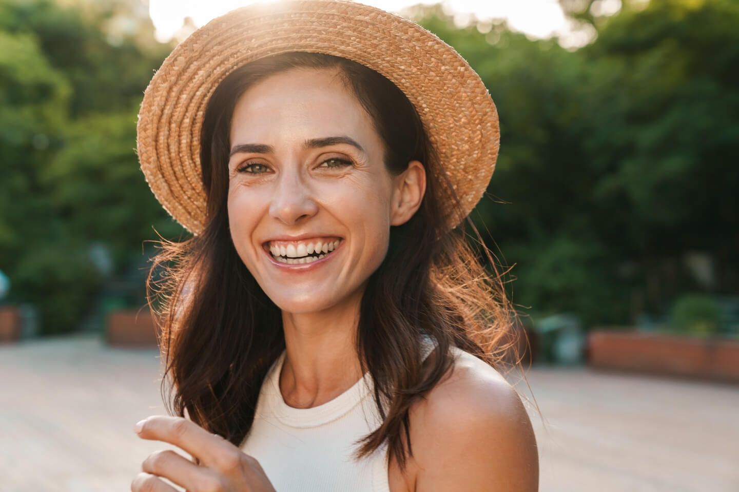 Image of beautiful middle-aged woman laughing and looking at camera while walking in summer park