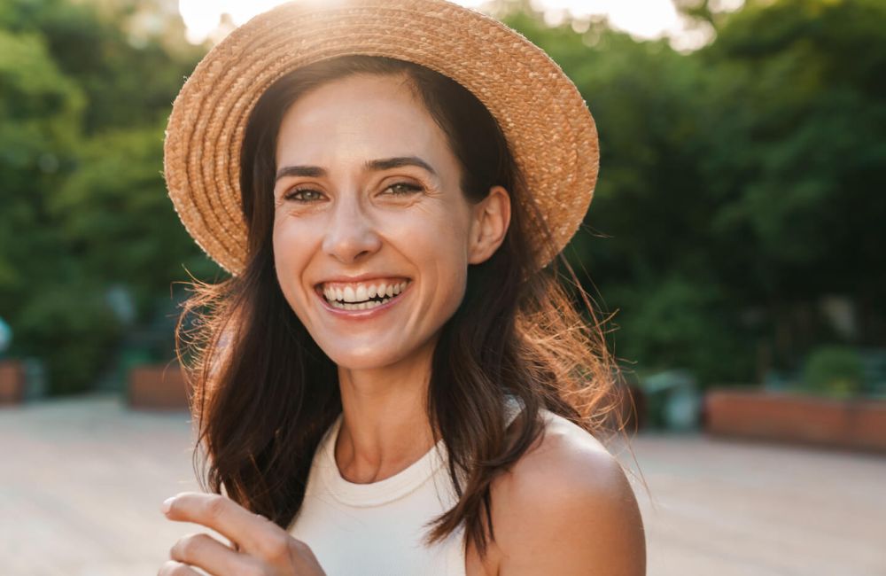 Image of beautiful middle-aged woman laughing and looking at camera while walking in summer park