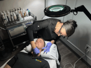 Esthetician performing skincare treatment on a man in a clinic with specialized lighting.