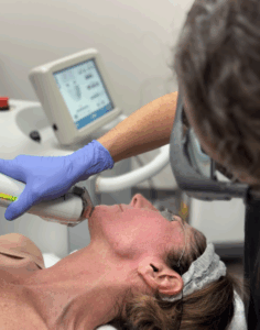 Person receives laser skin treatment in clinic setting, wearing safety goggles and headband.